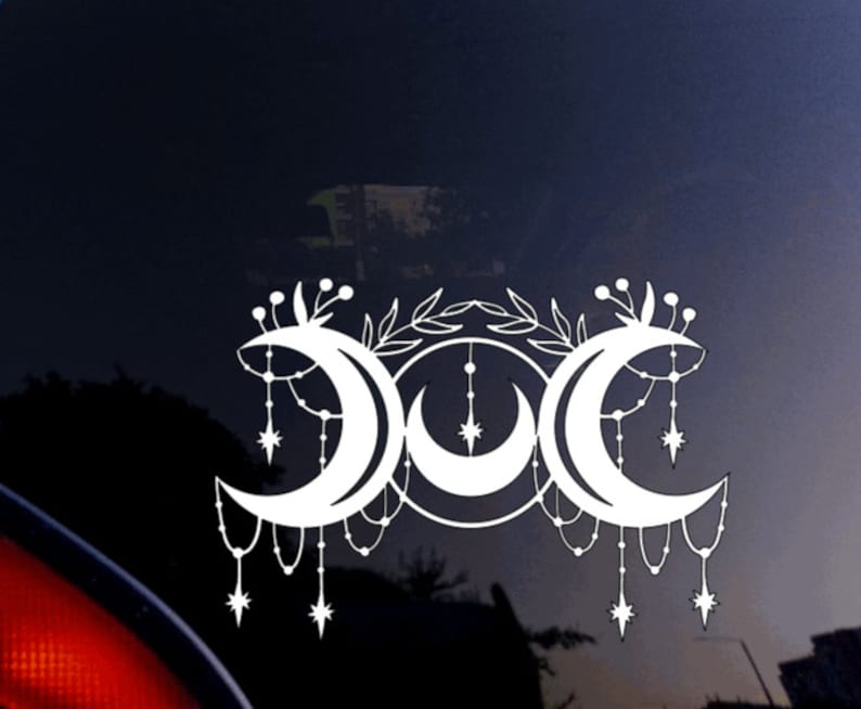May include: White vinyl decal of a triple moon symbol with a floral design and dangling stars. The moon phases are crescent, full, and waning crescent.