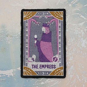 May include: Embroidered patch featuring "The Empress" tarot card design. The patch has a black border and depicts a figure in purple and pink robes, holding a scepter. The text "THE EMPRESS" is at the bottom, with gold and gray accents.