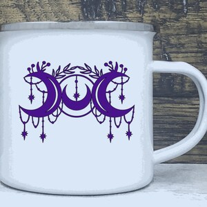 May include: White enamel mug with a purple triple moon design. The moon phases are surrounded by a floral design and dangling stars.