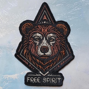 May include: Embroidered patch featuring a brown bear head with a geometric design and the text "FREE SPIRIT" in white.