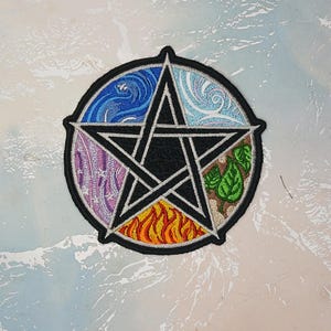 Peut inclure: Un pentacle noir à cinq branches, chaque branche représentant un élément : l’eau, l’air, la terre, le feu et l’esprit. Les éléments sont représentés par des broderies colorées autour du pentacle.