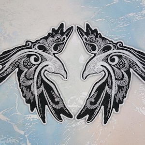 Könnte beinhalten: Zwei gestickte schwarze und weiße Patches von stilisierten Vögeln mit komplizierten Details. Die Vögel schauen sich mit ausgebreiteten Flügeln an.