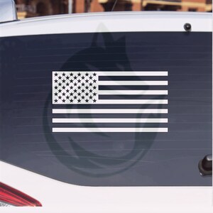 May include: A white American flag decal on a car window. The flag has 13 red and white stripes and a blue field with 50 white stars.
