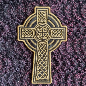 May include: A gold and black Celtic cross patch with intricate knotwork designs. The patch is embroidered and has a circular border.