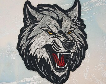 Könnte beinhalten: Gestickter Aufnäher mit einem knurrenden Wolfskopf. Der Wolf hat graues und weißes Fell, gelbe Augen und einen roten Mund. Der Aufnäher ist schwarz umrandet.