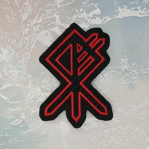 Pode incluir: Patch bordado vermelho e preto com um design geométrico. O patch tem a forma de um diamante e tem um fundo preto com um contorno vermelho.