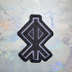 Puede incluir: Un parche bordado negro y gris con un diseño geométrico. El diseño es un símbolo estilizado con una forma de diamante en el centro y cuatro brazos que se extienden desde el centro.