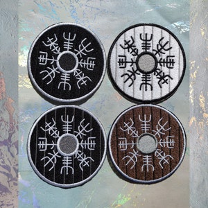 Puede incluir: Cuatro parches bordados con un diseño circular. Cada parche presenta un símbolo blanco sobre un fondo de color diferente: negro, blanco, marrón y gris.