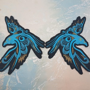 Könnte beinhalten: Zwei aufgestickte Aufnäher in Flügelform. Sie haben einen schwarzen Umriss mit detaillierten Mustern in Blau und Gold. Das Design ist stark stilisiert und verziert.