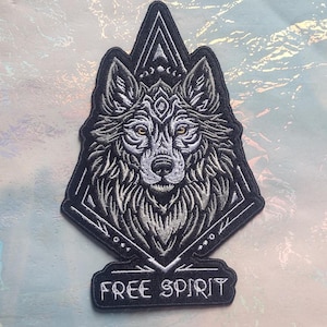 May include: Black and white embroidered patch featuring a wolf's head with a geometric design and the text "FREE SPIRIT".