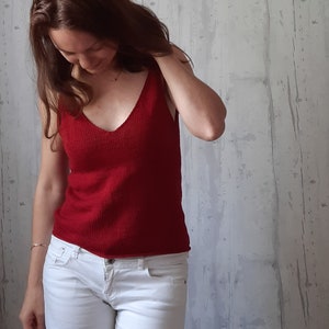 May include: A woman wearing a red sleeveless knitted top and white denim shorts.