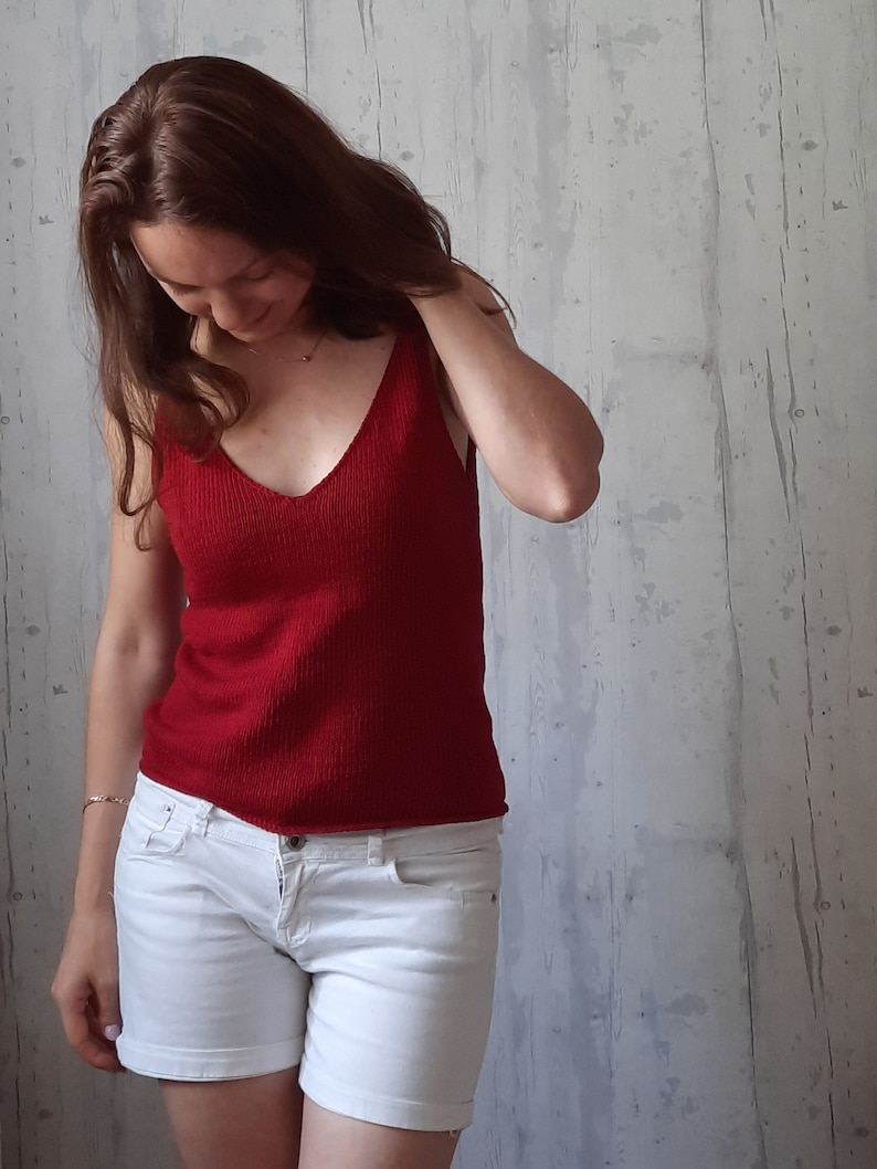 May include: A woman wearing a red sleeveless knitted top and white denim shorts.