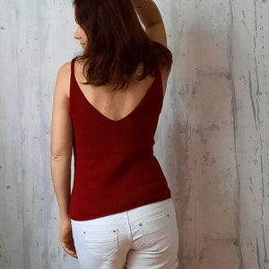 May include: A woman wearing a red tank top and white denim shorts. The tank top has a deep V-neck and a ribbed texture.