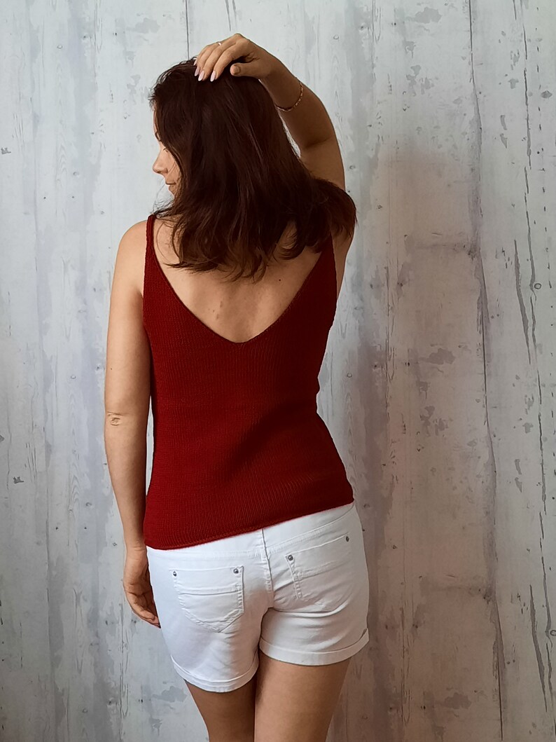 May include: A woman wearing a red tank top and white denim shorts. The tank top has a deep V-neck and a ribbed texture.