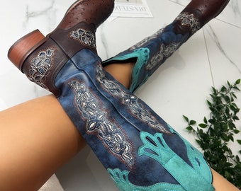 Pode incluir: Botas de cowboy azuis e marrons com bordados turquesa e prateados. As botas são de altura de joelho e têm uma ponta pontiaguda.