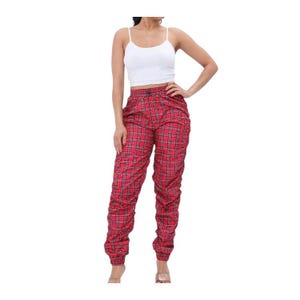 May include: Red plaid trousers with a gathered design. The trousers have a high waist and a relaxed fit. The plaid pattern is a classic design, with red as the primary colour and black lines creating the plaid pattern. The trousers are paired with a white vest top.