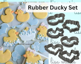 May include: A collection of yellow rubber ducky-themed cookies with blue and white accents, alongside matching cookie cutters. The cookies feature duck shapes, a bathtub, and bow details. The text "Rubber Ducky Set" is visible.