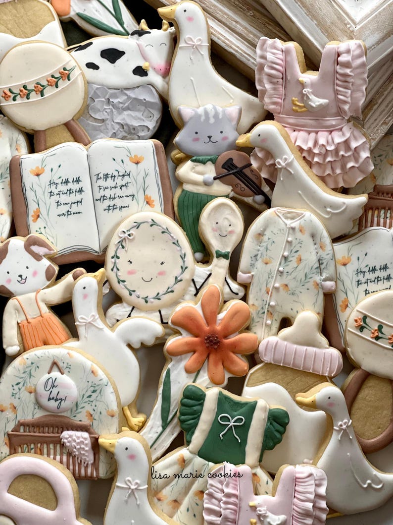 May include: A collection of decorated sugar cookies featuring a variety of baby-themed designs, including a cow, a goose, a flower, a book, a rattle, a spoon, a crib, and a dress. The cookies are decorated with pastel colors and floral patterns.