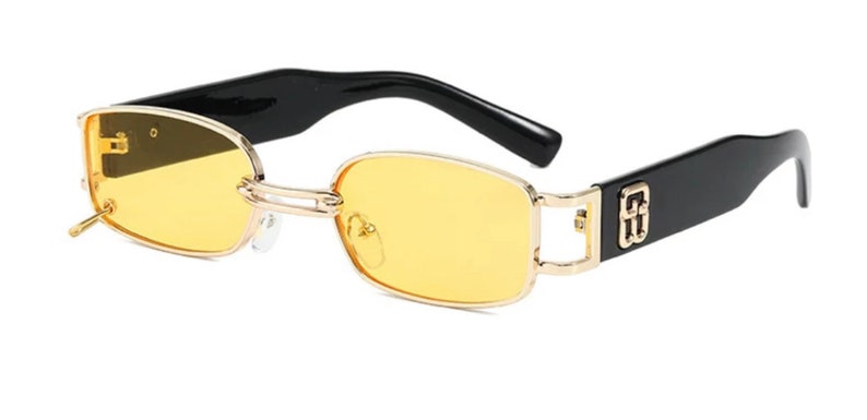 May include: Black and gold rectangular sunglasses with yellow lenses. The sunglasses have a logo on the side.