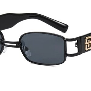 May include: Black rectangular sunglasses with a gold logo on the side. The sunglasses have a thin metal frame and dark lenses.