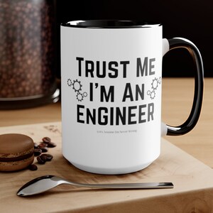 May include: White ceramic mug with a black rim and handle. The mug has black text that reads "TRUST ME I'M AN ENGINEER" with a small gear graphic on either side of the word "AN". Below the text is a smaller line of text that reads "Let's Assume I'm Never Wrong".