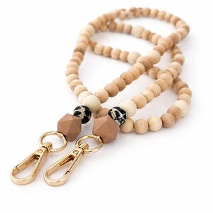 Könnte beinhalten: Ein Holzperlen-Lanyard mit goldfarbenen Verschlüssen. Das Lanyard hat hellbraune und cremefarbene Holzperlen, geometrische braune Perlen und Perlen mit einem schwarz-weißen Tiermuster. Entworfen für Schlüssel oder Ausweis.