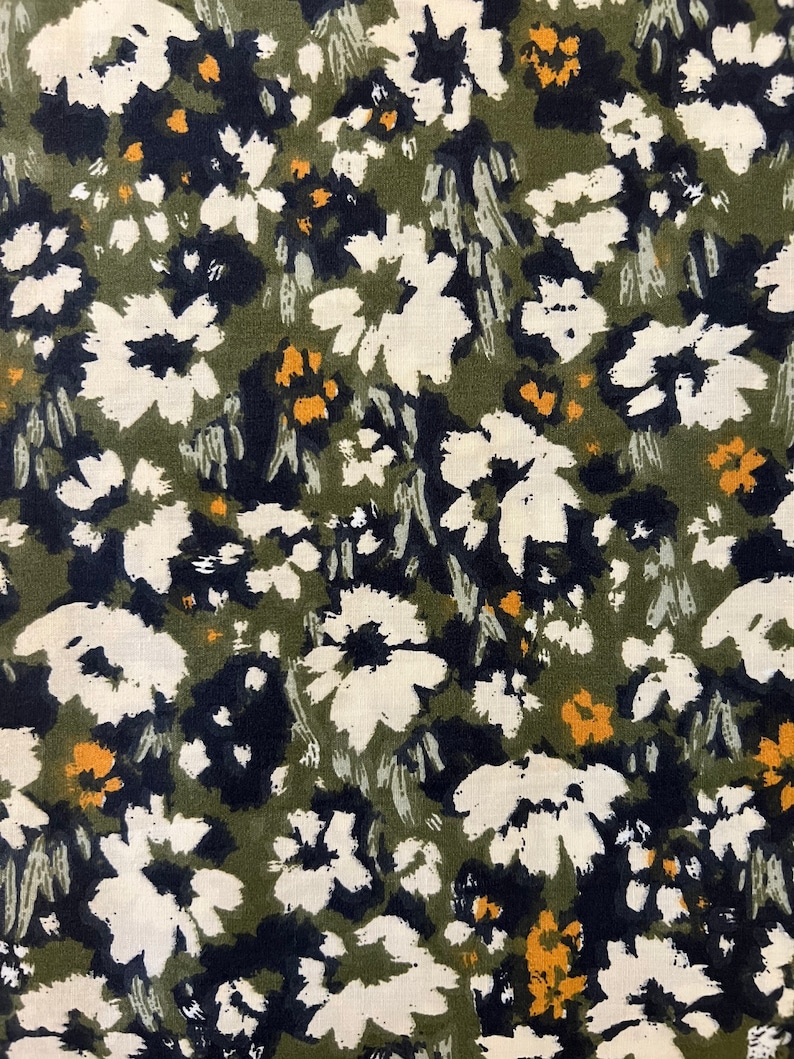 May include: Close-up of a fabric with a floral pattern. The design features white, navy, and yellow flowers scattered across an olive green background. The flowers have a brushstroke style, creating a textured appearance.