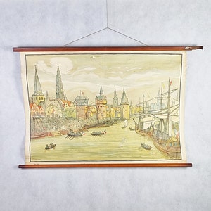 May include: A vintage educational poster depicting a cityscape with tall buildings and ships sailing on a body of water. The poster is framed in a wooden frame with a brown rope hanging from the top.