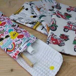 Peut inclure: Une pochette zippée rose et blanche avec un imprimé graphique coloré comportant le texte "You got this" et "Girl power". La pochette est ouverte et contient une brosse à dents et du dentifrice. La pochette est posée sur une surface en bois.