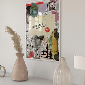 May include: A framed collage art print featuring vintage imagery. The artwork includes a yellow car, ice cream, a postcard with the text "Meet Me in New York," and a red kiss mark. The print is displayed on a white wall.