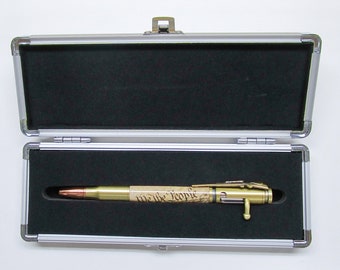 May include: A gold-colored pen made from a bullet casing with the text "We the People" inscribed on the side. The pen is in a silver aluminum case with a black interior.