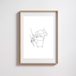 May include: A framed minimalist line art print featuring a koala bear hugging a tree branch. The koala is depicted with a simple, continuous black line, conveying a sense of calm and simplicity. The artwork is set against a white background.
