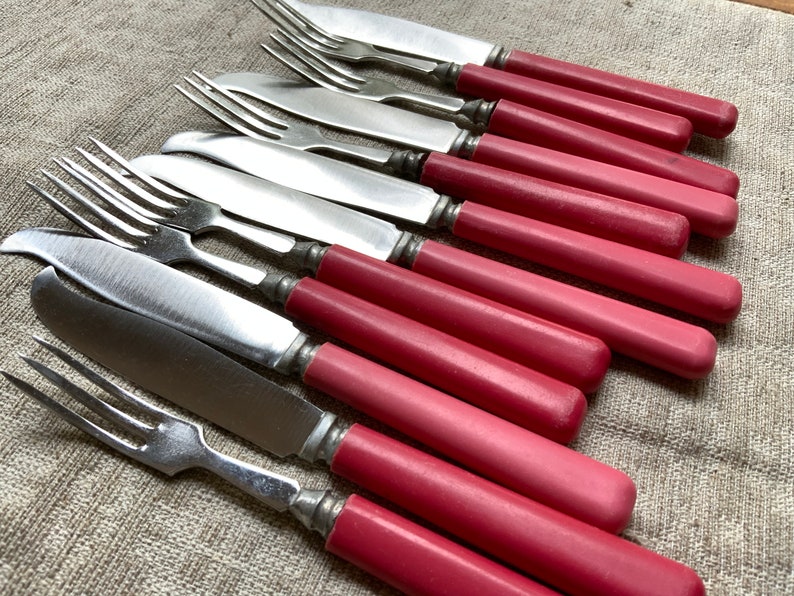 Op de afbeelding: Een set vintage zilveren bestek met roze kunststof handvatten. De set bevat zowel vorken als botermesjes.