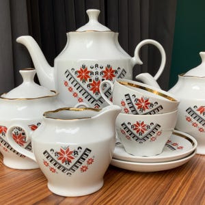 Peut inclure: Service à thé en porcelaine blanche comprenant une théière, un sucrier, une crémière et des tasses. L'ensemble présente un motif géométrique rouge, noir et blanc avec des bordures dorées. L'ensemble comprend une théière, un sucrier, une crémière et des tasses.