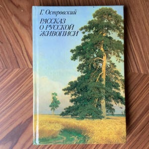 Op de afbeelding: Een boek met een landschapsschilderij op de omslag. Het kunstwerk toont een hoge den in een veld met tarwe onder een blauwe lucht. De titel van het boek is in het Russisch.
