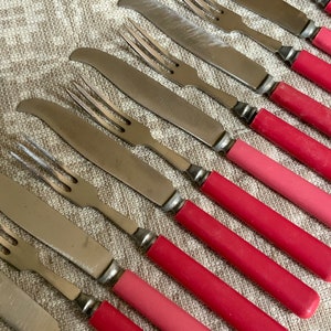 Op de afbeelding: Een set van roestvrijstalen messen en vorken met roze handvatten. De handvatten zijn een gradi&euml;nt van roze, van licht naar donker.