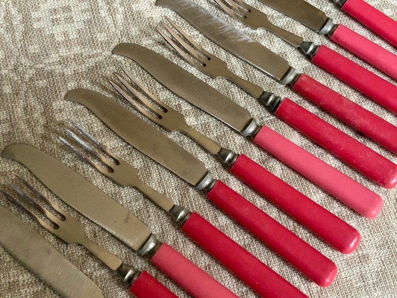 Op de afbeelding: Een set van roestvrijstalen messen en vorken met roze handvatten. De handvatten zijn een gradi&euml;nt van roze, van licht naar donker.