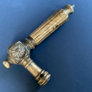 Könnte beinhalten: Antiker Türgriff aus Messing mit detailliertem Blumendesign auf der quadratischen Basis. Der Griff hat einen geriffelten Griff und ein kleines Loch am Ende. Das Messing hat eine verwitterte Patina.
