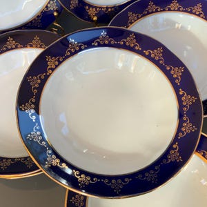 Op de afbeelding: Een verzameling witte porseleinen kommen met een donkerblauwe rand. De blauwe rand is versierd met gouden filigraan ontwerpen. De kommen zijn in een close-up geplaatst, wat hun elegante ontwerp en vakmanschap benadrukt.