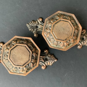 Puede incluir: Dos tiradores de puerta o armario de latón antiguo con diseños octogonales ornamentados. Los tiradores tienen un acabado texturizado envejecido y detalles florales intrincados.