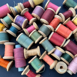May include: A collection of wooden spools of thread in various colors, including red, green, blue, orange, and yellow. The spools are arranged in a random pattern on a dark blue surface.