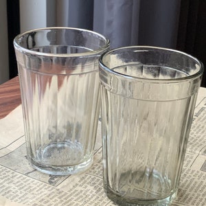 Puede incluir: Dos vasos transparentes de vidrio con un diseño acanalado. Los vasos están vacíos y se encuentran sobre un periódico.