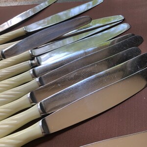 May include: A set of ten silver dinner knives with ivory-coloured twisted handles. The knives are arranged in a stack, with the blades facing up.