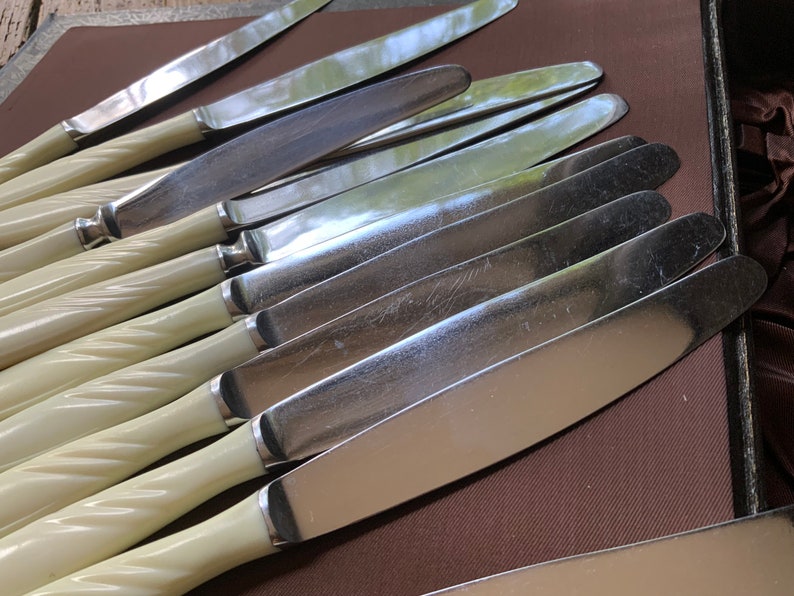 May include: A set of ten silver dinner knives with ivory-coloured twisted handles. The knives are arranged in a stack, with the blades facing up.