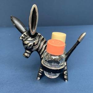 Puede incluir: Un juego de salero y pimentero vintage con forma de cebra. La cebra es negra y plateada, sosteniendo dos saleros de vidrio con tapas de color naranja y crema. Un accesorio único para la cocina o la mesa del comedor.