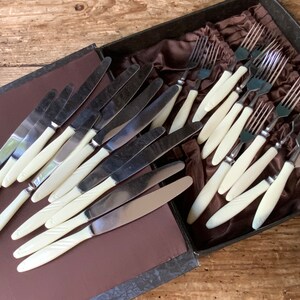 May include: A set of vintage silver cutlery with ivory handles in a brown velvet lined box. The set includes knives and forks.