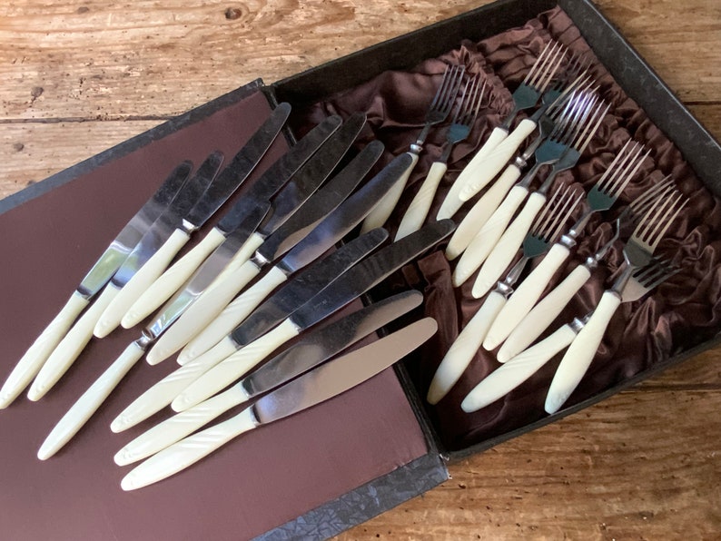 May include: A set of vintage silver cutlery with ivory handles in a brown velvet lined box. The set includes knives and forks.