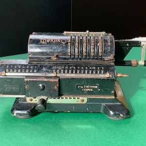Puede incluir: Una máquina de sumar mecánica vintage negra con el texto "Феликс" y "3-д СЧЕТМАШ КУРСК" en la parte delantera. La máquina tiene una palanca en el lado derecho y una serie de diales numerados en la parte superior.