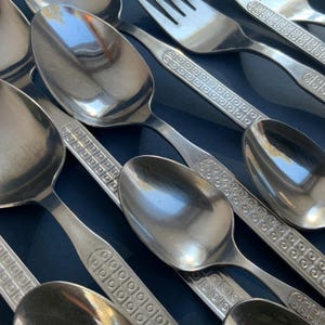 May include: Close-up of stainless steel silverware, including spoons and a fork. The silverware has a decorative pattern on the handles and a shiny, reflective surface. The arrangement suggests a set of dining utensils.
