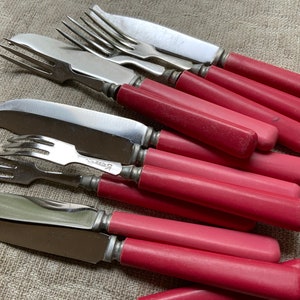 Op de afbeelding: Een set vintage bestek met roze handvatten, inclusief vorken en messen. De handvatten zijn van een levendige roze kleur en het metaal is glanzend en zilver.